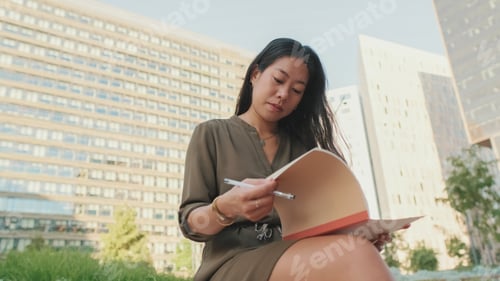 Preview: Young girl looks through notes in notebook while sitting on modern buildings background