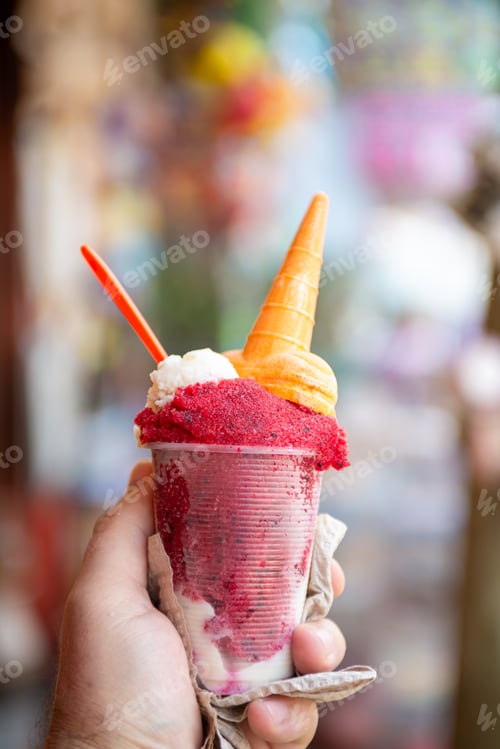 Preview: Hand holding delicious pitaya ice cream with cone and garnish.