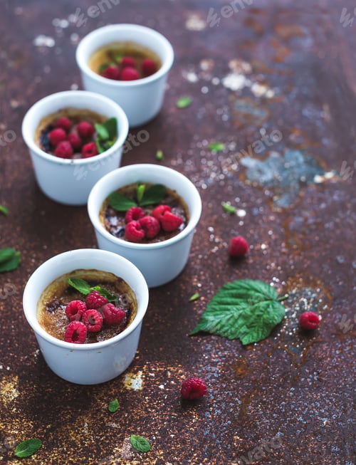Preview: Creme brulees with raspberries and mint in white bowls over grunge metal backdrop. Top view