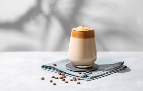 Preview: Dalgona coffee. Whipped instant coffee in a glass with beans and shadow on a light background.
