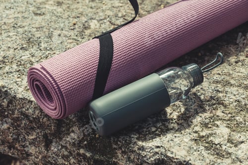 Preview: A yoga mat and a bottle of water resting over a rock with copy space