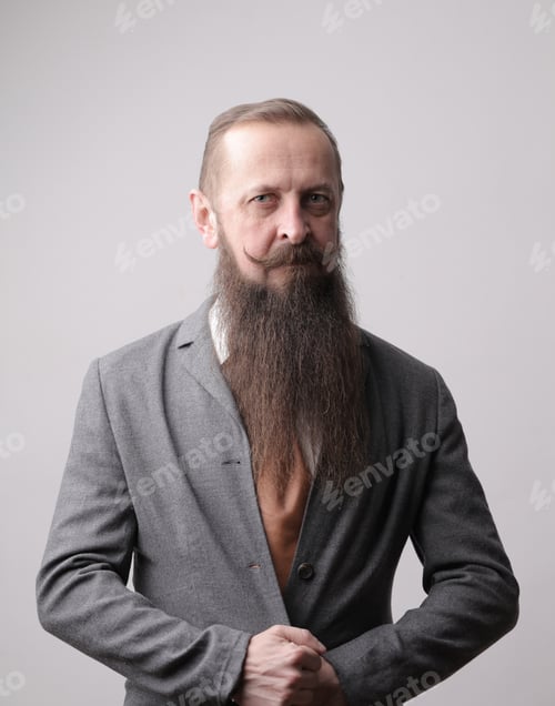 Preview: Vertical shot of a man with a long beard and a mustache standing in front of a grey wall