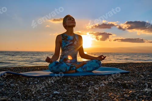 Preview: Young woman practicing yoga on the beach at sunrise.