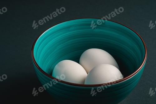 Preview: White eggs in green bowl on dark moody black plain minimal background, angle view, happy Easter day