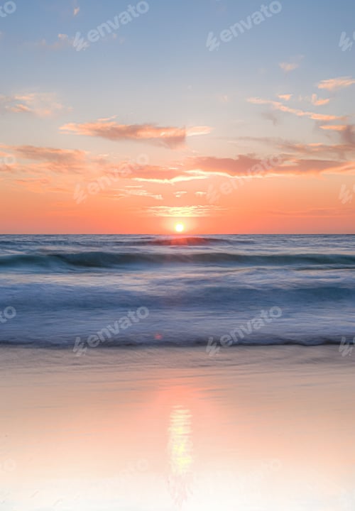 Preview: A colourful sunrise over the ocean. Reflection in the sand and an orange horizon