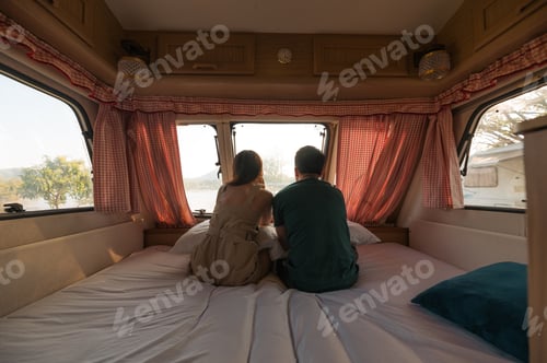 Preview: Young couple sitting and taking a view on mattress inside of camper van