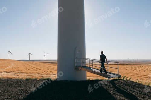 Preview: A wind farm technician standing and using a laptop at the base of a turbine on a wind farm in open