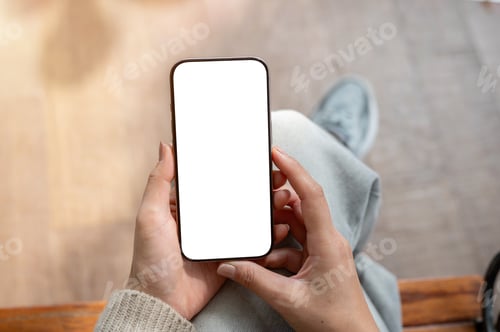Preview: A top view of a woman sits indoors and holds a smartphone with a white screen mockup.