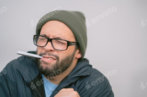 Preview: Sick young man with thermometer in mouth feeling cold