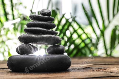 Preview: Table with stack of stones and blurred green leaves on background, space for text. Zen concept