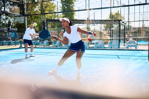Preview: Black athletic woman playing padel in mixed doubles on outdoor court.