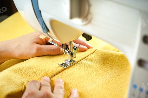 Preview: Female hands stitching yellow fabric on modern sewing machine. Close up view of sewing process.