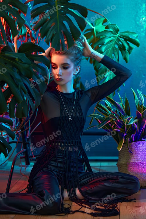 Preview: Young woman surrounded by vibrant tropical plants, wearing black leather outfit and long-sleeved