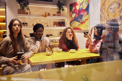 Preview: Mixed race happy young people gathering in cafe, sitting at table, chatting, talking, drinking