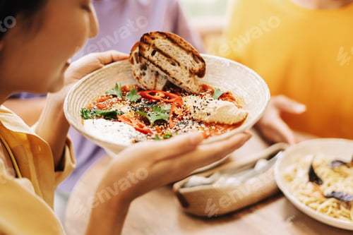 Preview: Woman holding bowl of shakshuka with friends at restaurant