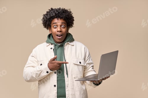 Preview: Surprised African guy holding laptop pointing at computer advertising wow offer.
