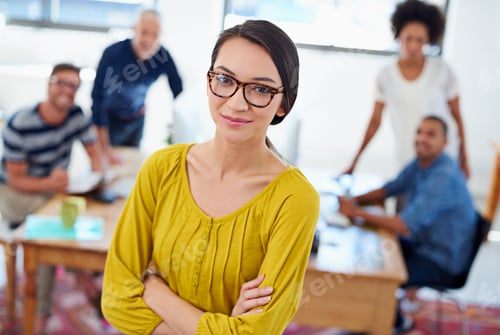 Preview: Young confident businesswoman looking at the camera with coworkers in the background