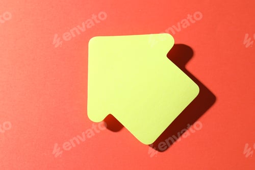 Preview: One yellow paper arrow on red background, top view