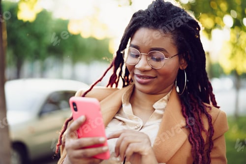 Preview: African american woman standing in a street and using smartphone