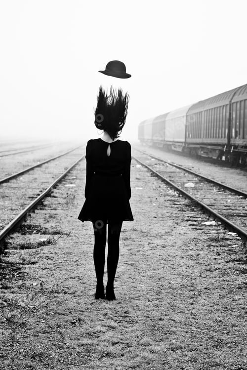 Preview: Vertical shot of a female standing between railroads with her hat flying off