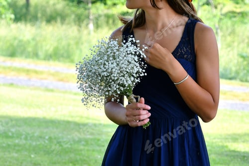 Preview: A bridesmaid in a blue gown holding a bouquet of baby's breath flowers outside.