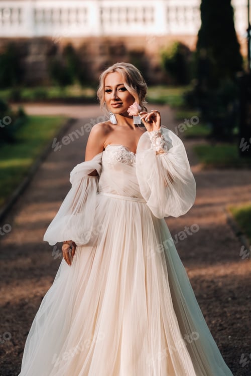 Preview: Beautiful bride in a luxurious wedding dress holds a bouquet of white roses and greens on a green