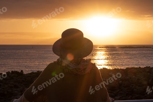 Preview: Back view of woman silhouette with hat admiring the orange sunset over the sea. Love and peace