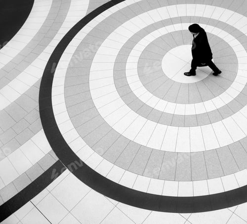 Preview: High angle view of man wearing coat and hat walking across tiled floor with circular pattern.