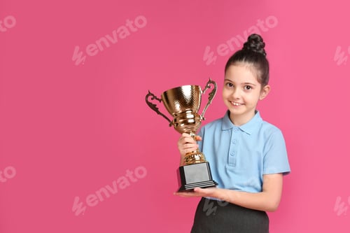 Preview: Happy girl in school uniform with golden winning cup on pink background. Space for text