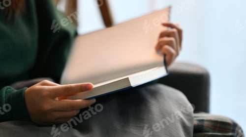 Vista previa: Carefree young woman in warm sweater reading book on comfortable couch at home