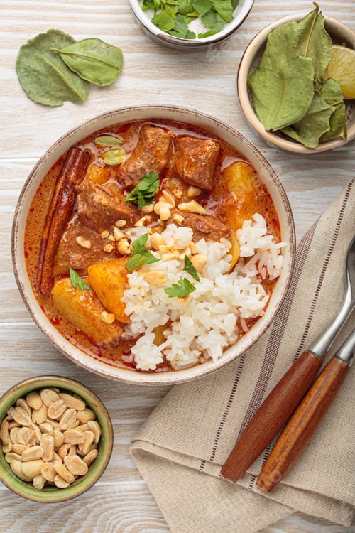 Preview: Delicious massaman curry with beef, potatoes, rice, and peanuts on white wooden background