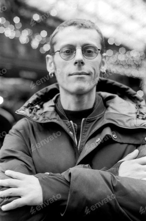 Preview: Man wearing glasses and winter jacket crossing arms in blurred background with bokeh effect