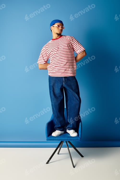 Preview: Stylish young man in beanie and striped shirt striking a pose against a blue backdrop