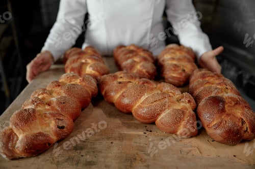 Preview: Woman baker holding tray with freshly baked braided bun