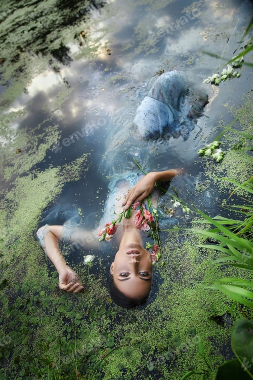 Visualização: Arte linda mulher romântica encontra-se no pântano no vestido longo azul com flores. Morena de retrato em