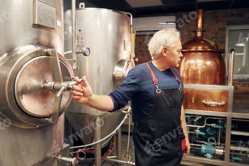 Preview: Senior man is standing in the storage with equipment for beer