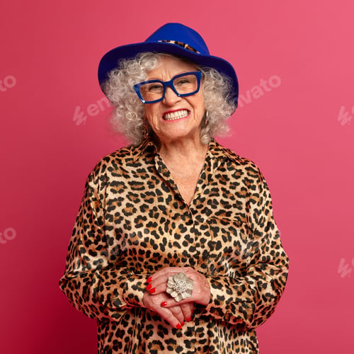 Preview: Happy grandmother smiles toothily, wears fashionable blue hat and leopard outfit, looks through tran