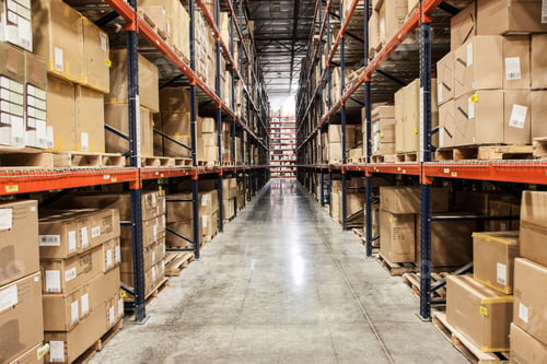 Preview: View down an aisle of racks holding cardboard boxes of product on pallets in a large distribution