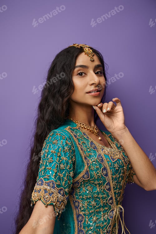 Preview: beautiful indian woman in traditional blue sari posing on purple backdrop and looking at camera