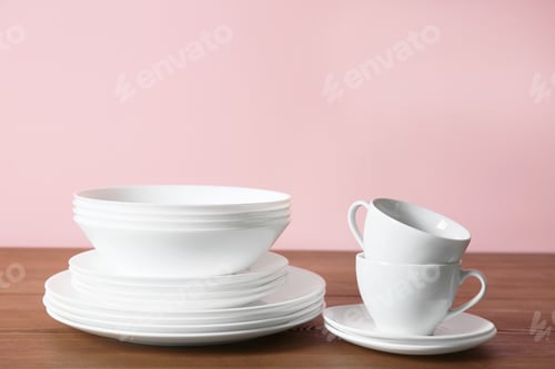 Preview: Set of clean dishes on table against color background