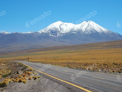 Preview: Beautiful shot of an empty road surrounded by fields and mountains covered in snow during daylight