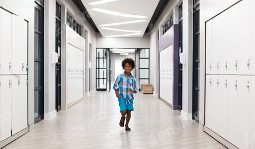 Preview: Full length of smiling african american elementary schoolboy running in corridor with lockers