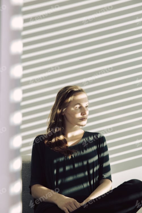 Preview: Portrait of serious young woman sitting in a shadowed room