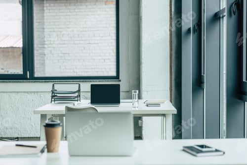 Preview: office desks with laptops, coffee to go and glass of water, notebooks and documents tray