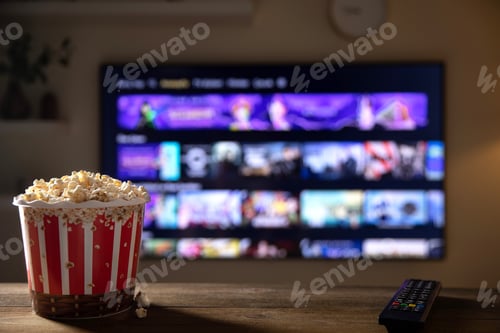 Preview: Close up of bowl of popcorn and remote control with TV works on background.