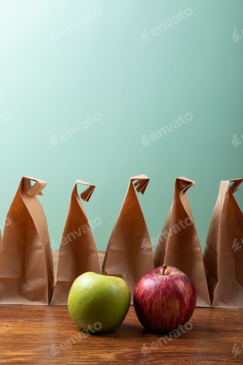 Preview: Apple and granny smith apple by paper lunch bags on table against green background with copy space