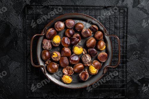 Preview: Cracked roast chestnuts served in a tray. Black background. Top view