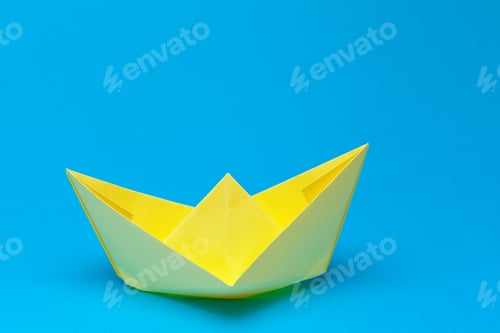 Preview: Colorful paper boat floats on a blue background during a sunny day
