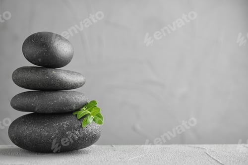 Preview: Stack of spa stones and green leaves on grey table, space for text