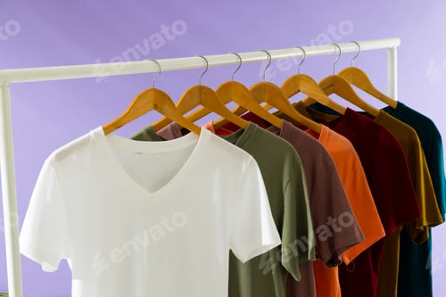 Preview: Coloured tshirts displayed on clothing rail and copy space on purple background